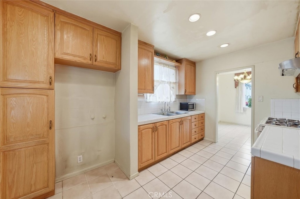 Kitchen with honey-colored wood cabinets, tiled floors, a double sink, and a gas range.