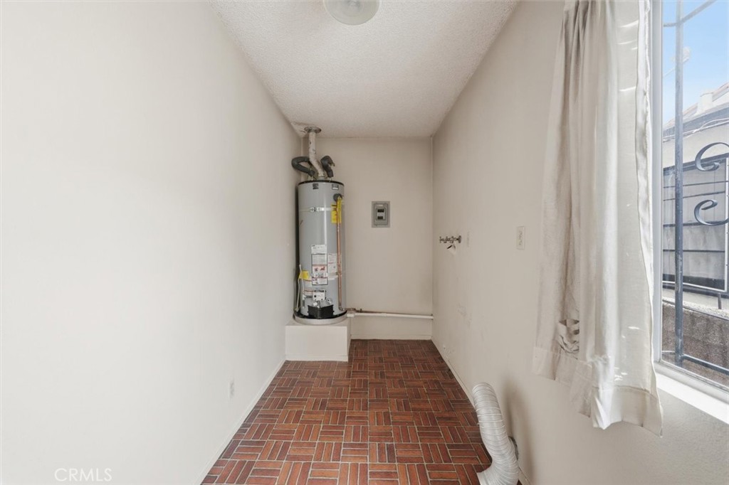 Utility room with a tank water heater, brick-pattern tile floor, and curtained window.