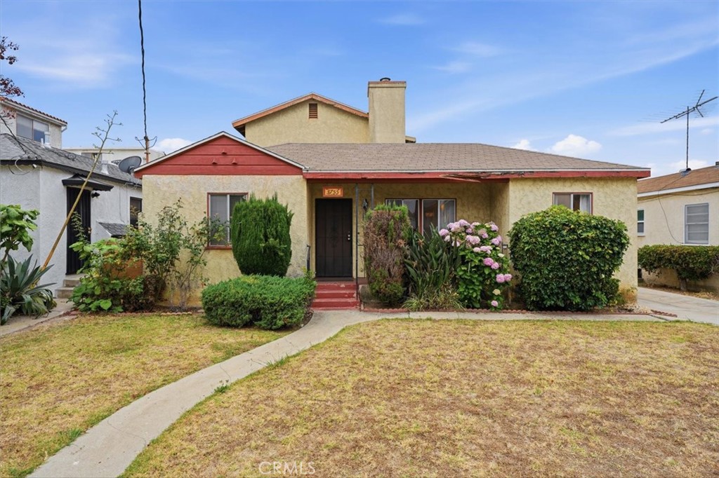 Single-story home with a red front gable, flowering shrubs, and a curved walkway across the front lawn.