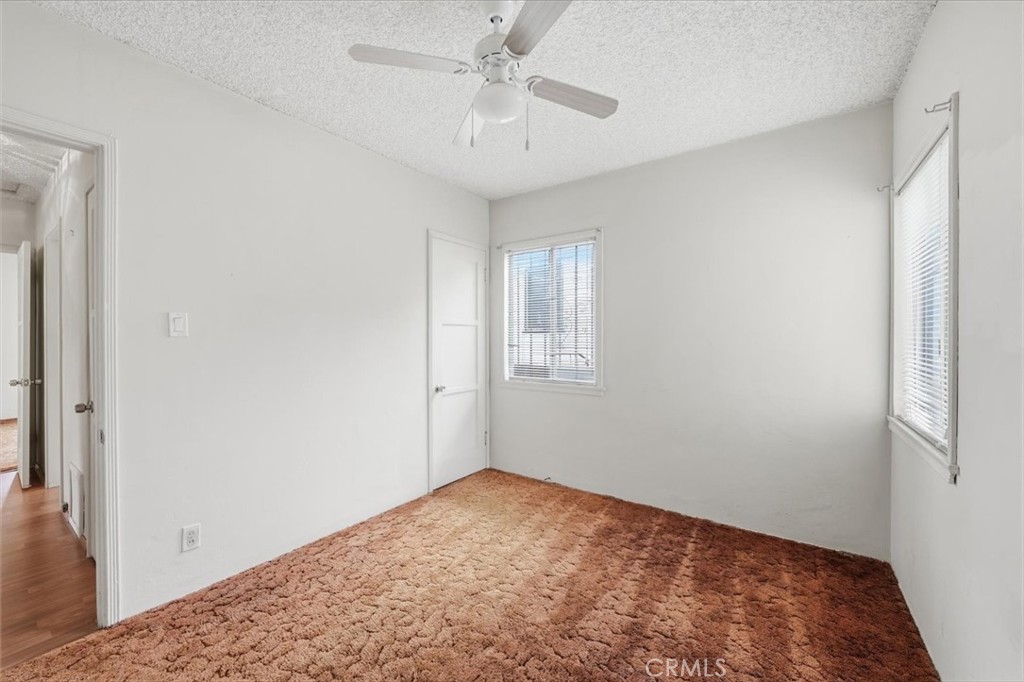 Empty bedroom with rust-colored carpet, two windows with blinds, and a ceiling fan.