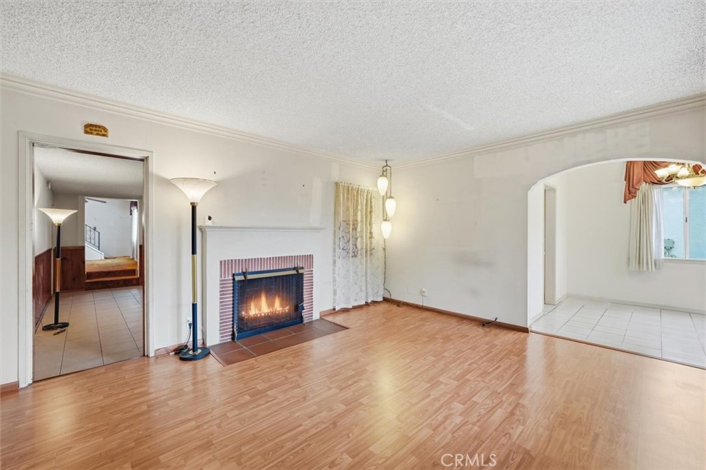 Vacant living room with a brick fireplace, wood-look floors, and an arched opening to a tiled room.
