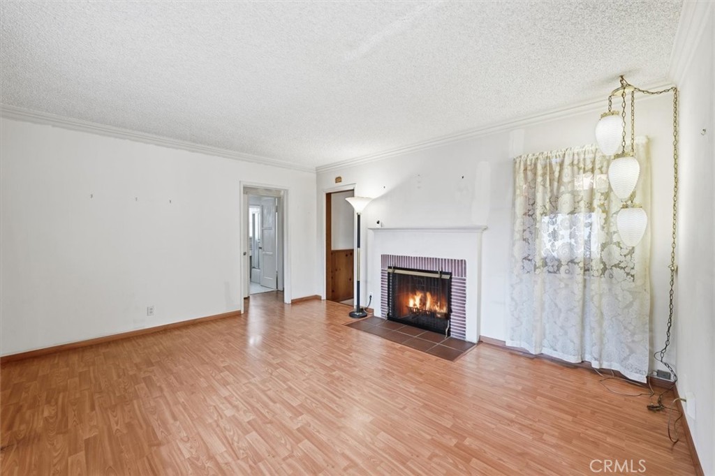 Unfurnished living room with a lit fireplace, light wood flooring, and lace curtains.