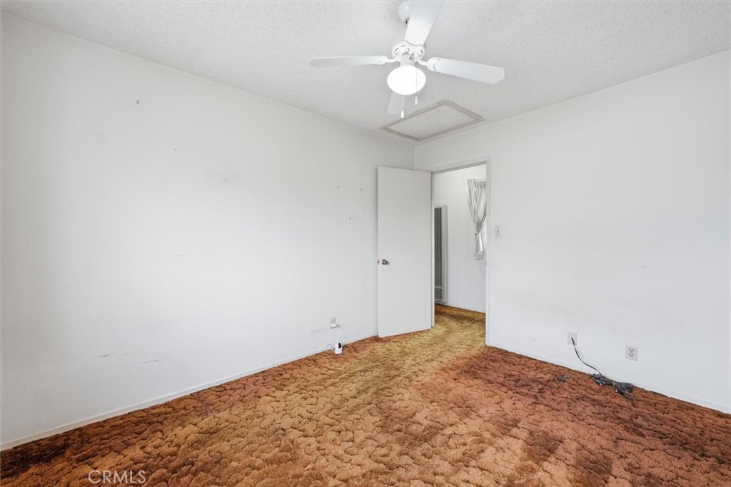 Empty bedroom with thick rust-colored carpet, a white ceiling fan, and an open doorway.