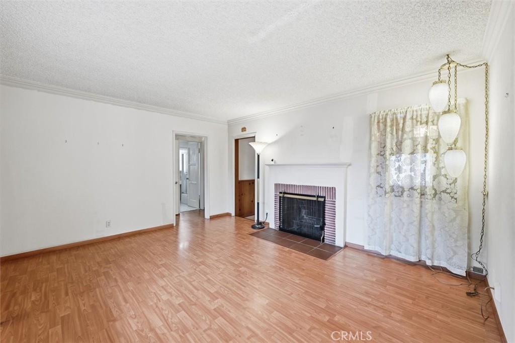 Mostly empty living room with a brick fireplace, wood-look flooring, and floral curtains.