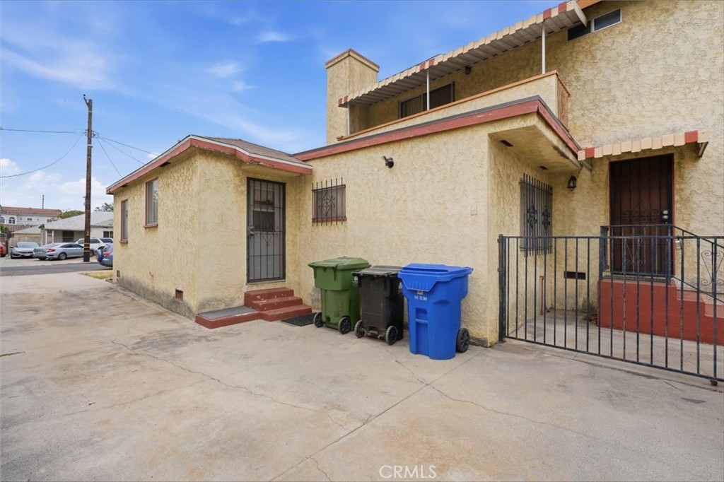 Beige stucco residence with red trim, barred entryways, and three bins beside the driveway.
