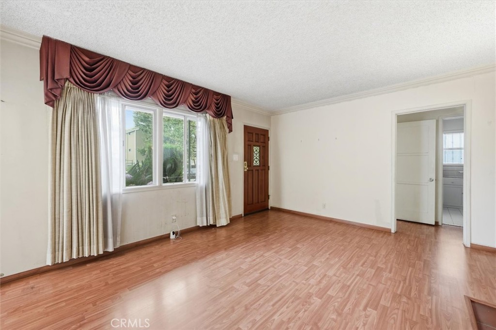 Empty living room with wood-look flooring and a large window dressed with layered curtains.