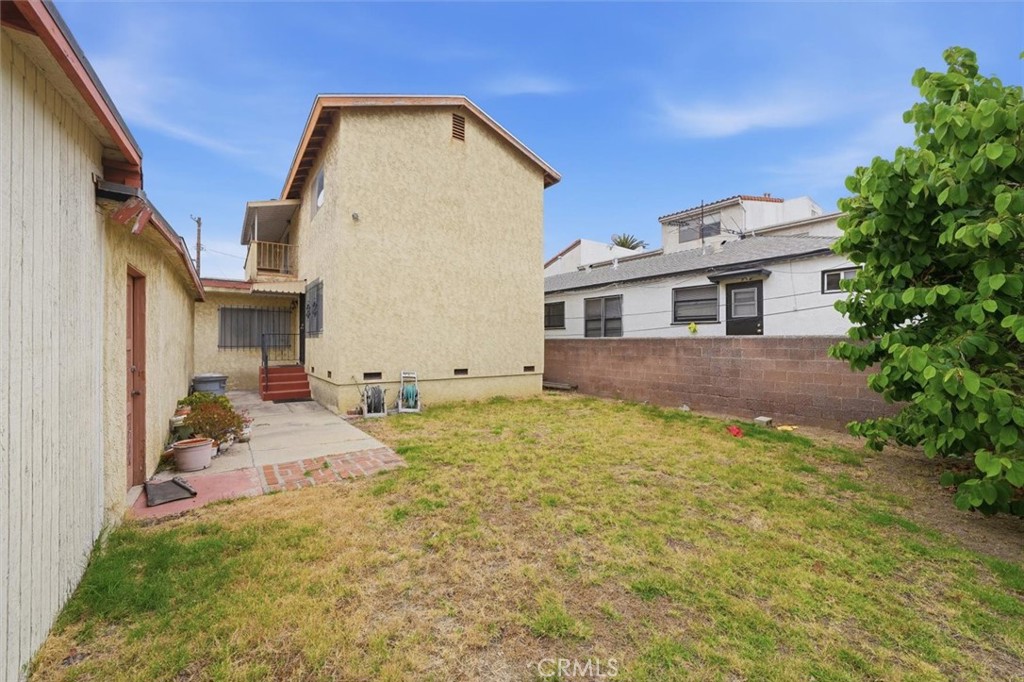 Rear yard with a patchy lawn, paved walkway, and beige stucco home.