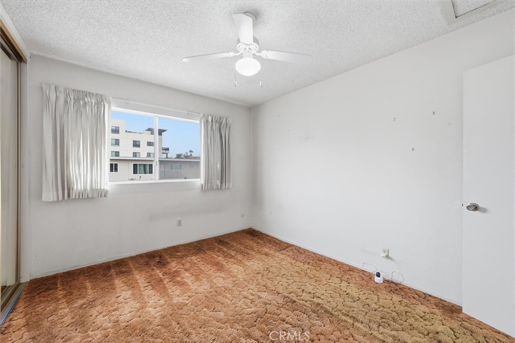 Empty bedroom with brown patterned carpet, curtained window, and white ceiling fan.