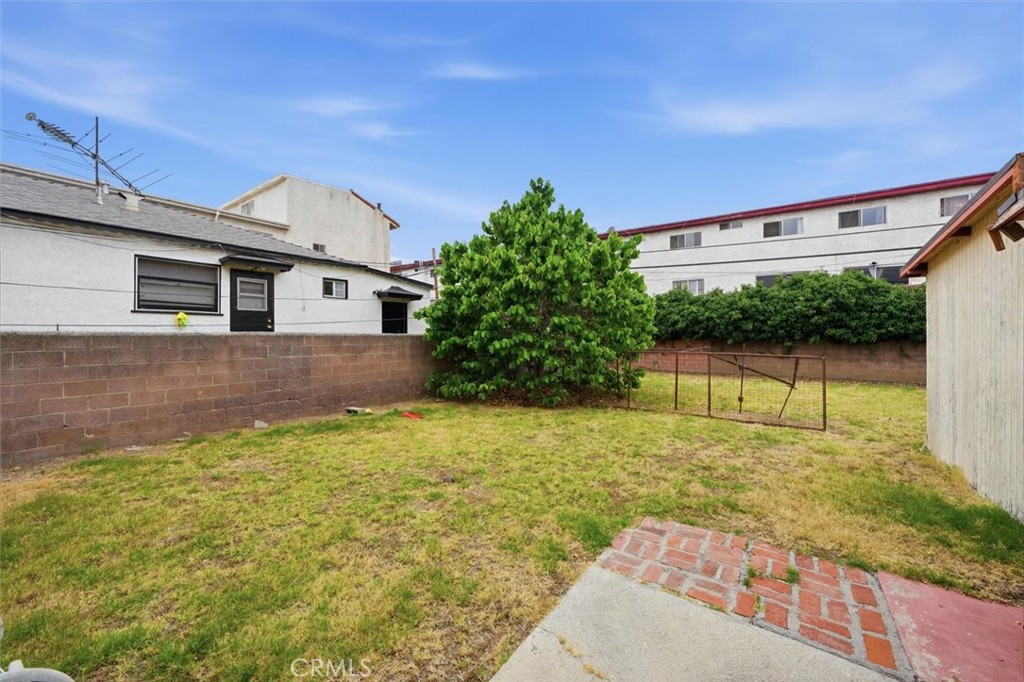 Backyard with a grassy lawn, large leafy tree, brick wall, and metal gate.