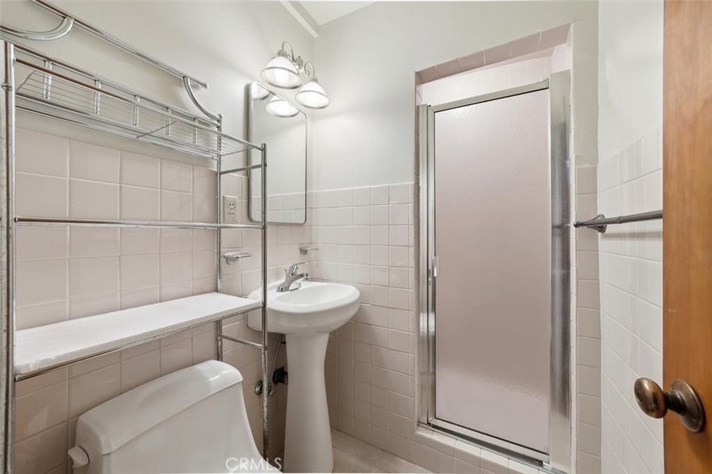 Bathroom with a frosted-glass shower, pedestal sink, toilet, and chrome shelving.
