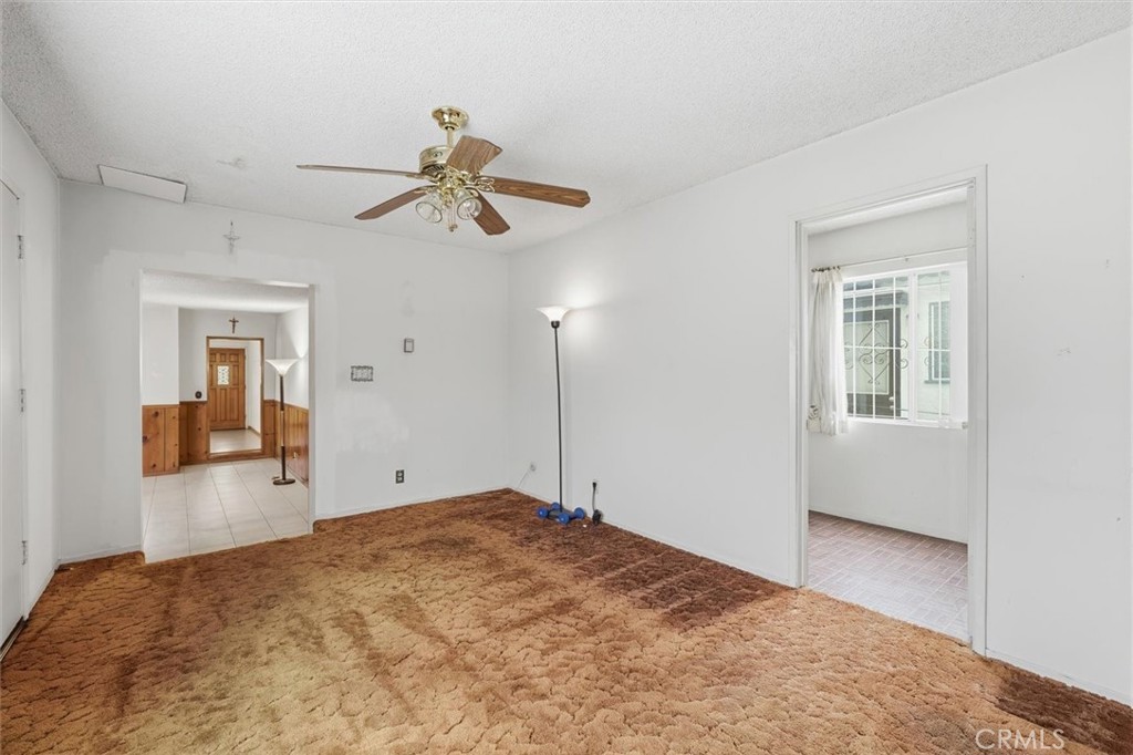 Unfurnished living room with thick brown carpet and a ceiling fan, opening to a tiled hall and another room.