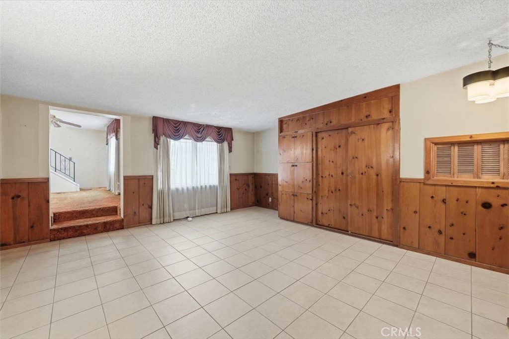 Empty tiled room with wood-paneled walls, built-in cabinets, and a curtained window.