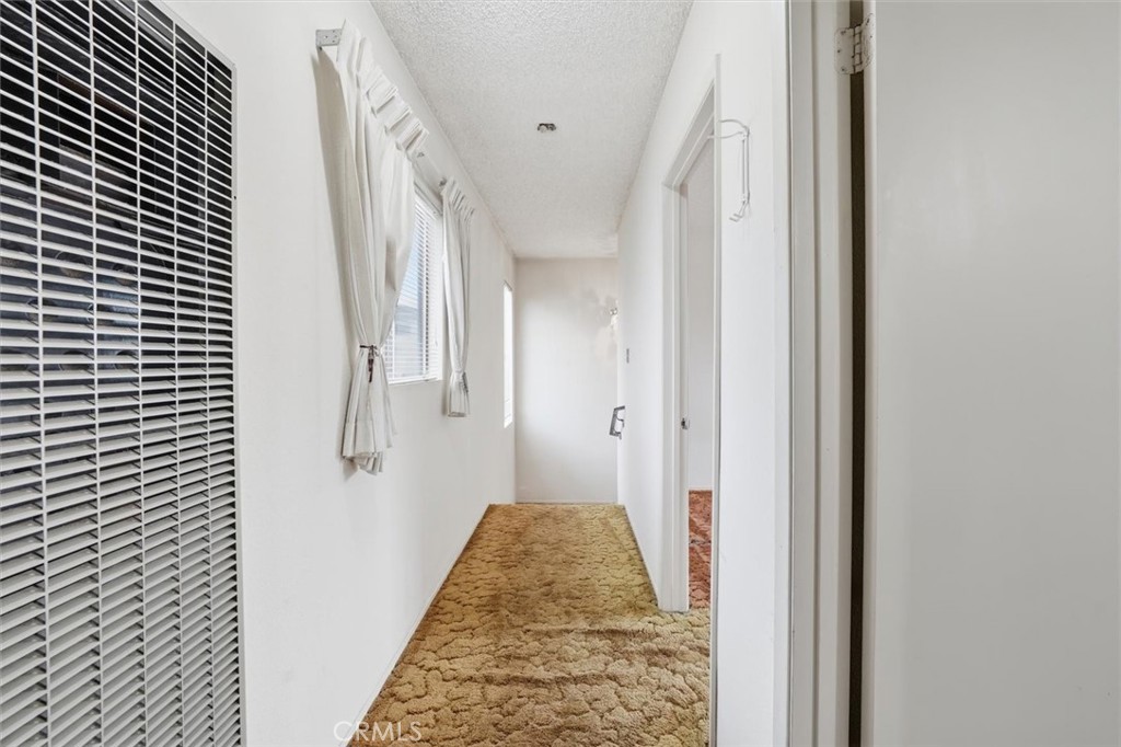 Narrow white hallway with tan textured carpet, curtained windows, and open doorways.