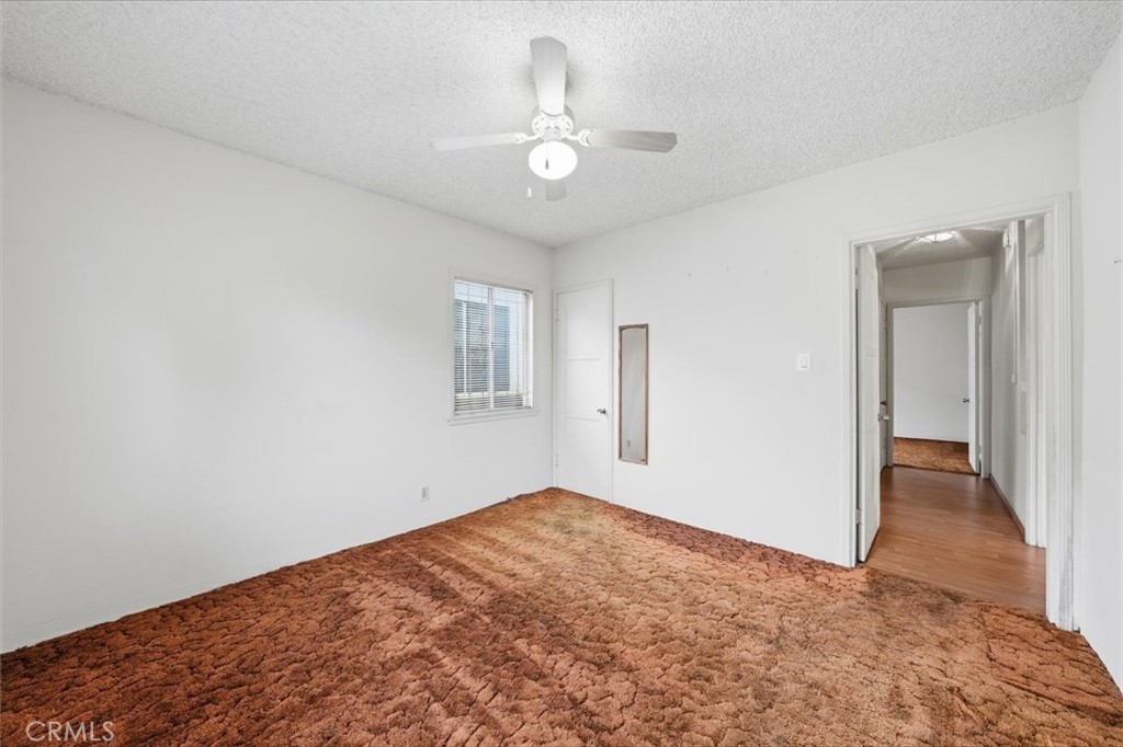 Unfurnished bedroom with rust-colored carpet, a ceiling fan, and a window with blinds.