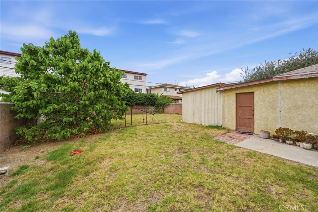 Backyard with a patchy lawn, leafy tree, metal gate, and small outbuilding.