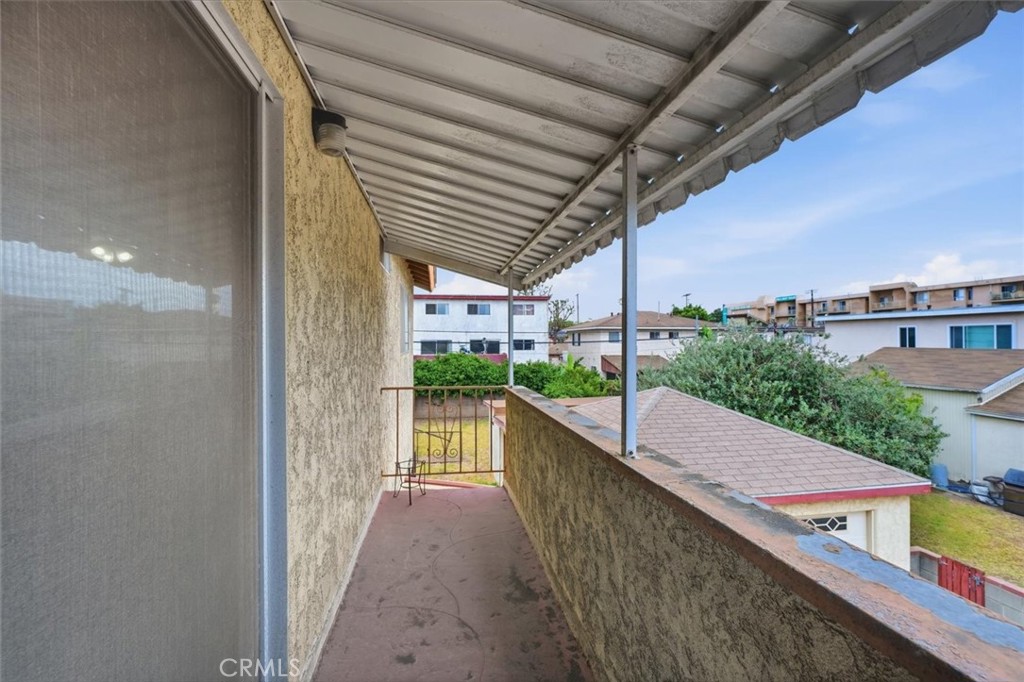 Covered balcony overlooking nearby homes, with a small metal chair and table at the far end.