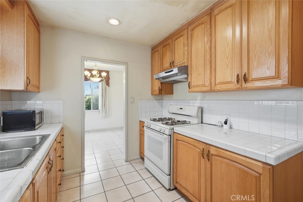 Kitchen with honey-colored wood cabinets, white tile counters, and a white gas range.