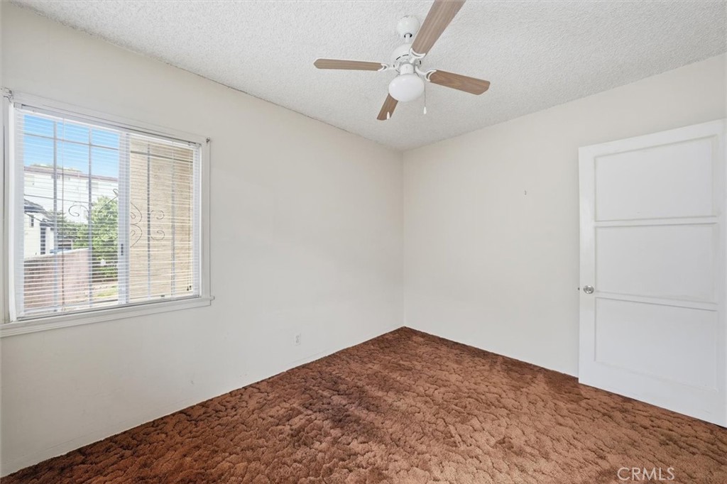 Empty bedroom with brown carpet, a window with blinds, and a ceiling fan.
