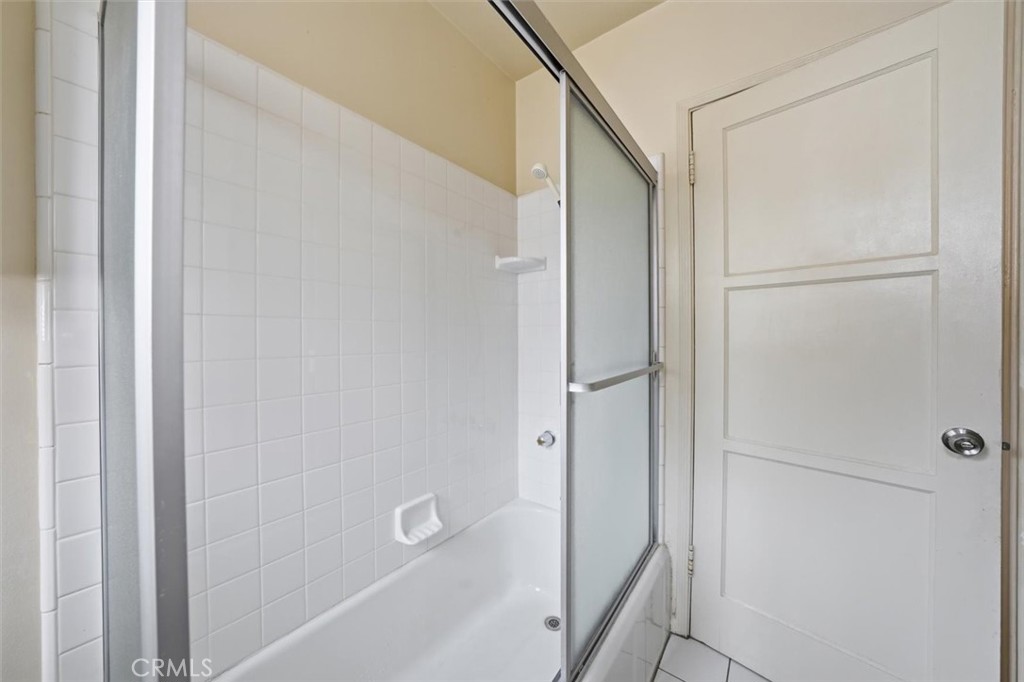 Bathroom with a white bathtub and tiled shower behind a sliding frosted-glass enclosure.