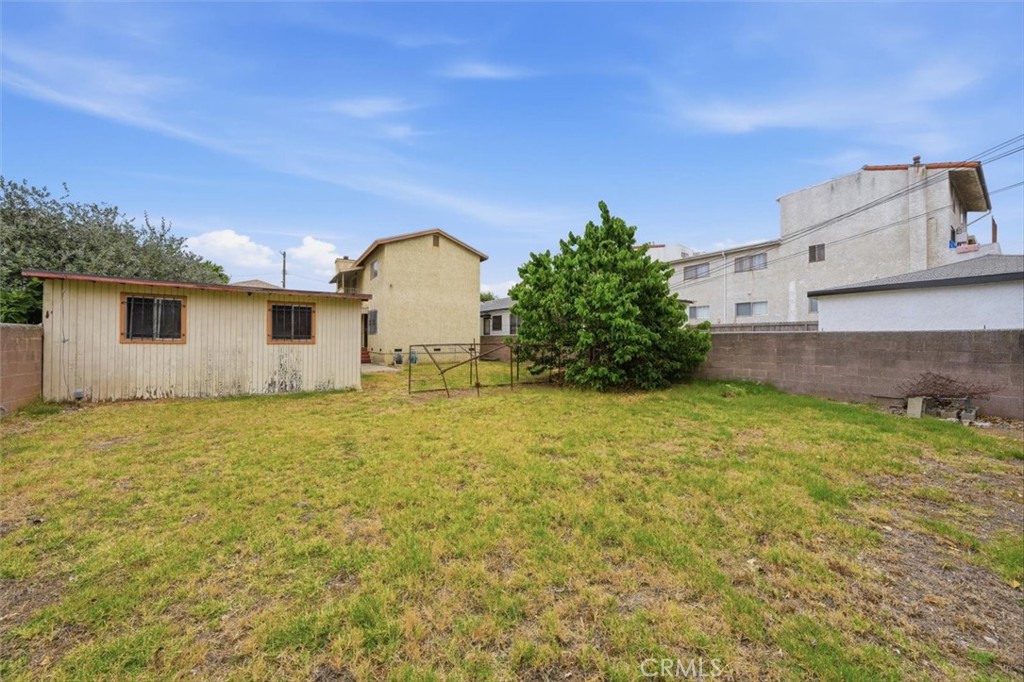 Grassy backyard with a detached shed, mature tree, and block perimeter wall.