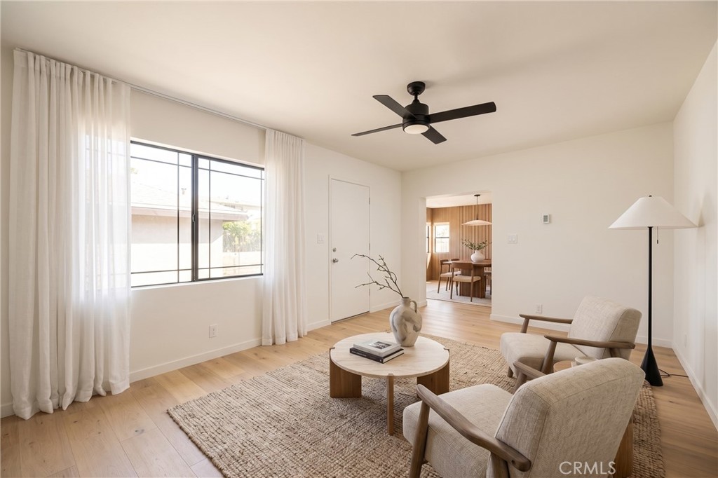 Living room with sheer-curtained window, upholstered armchairs, round coffee table, and light wood floors.