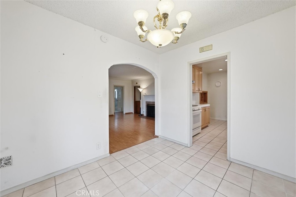 Dining area with tiled flooring, a chandelier, and arched opening to the living room.