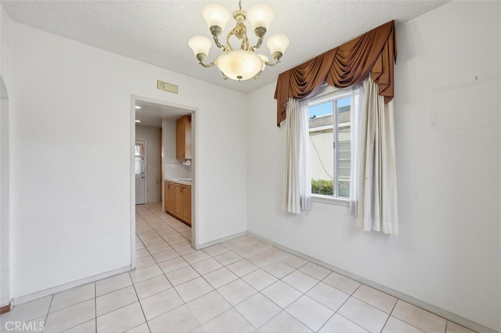 Unfurnished tiled dining area with a chandelier, curtained window, and doorway to the kitchen.