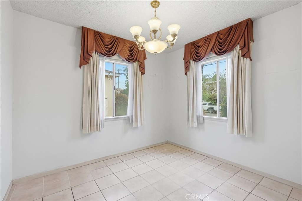 Empty dining room with tiled floor, two curtained windows, and a brass chandelier.