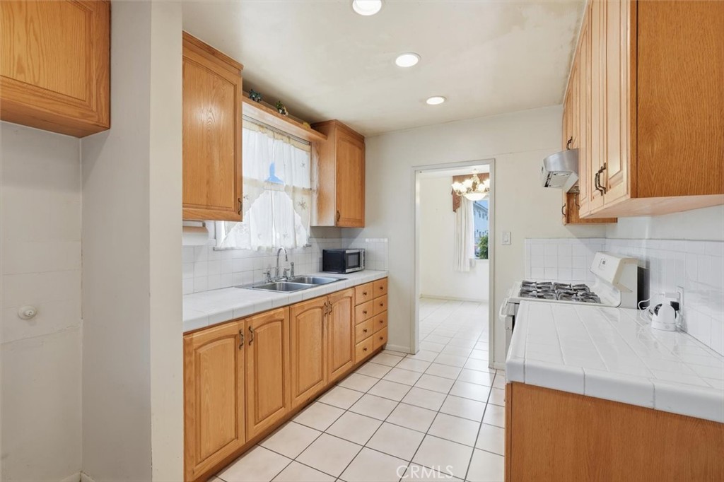 Kitchen with honey-colored wood cabinets, white tile counters, and a gas range.