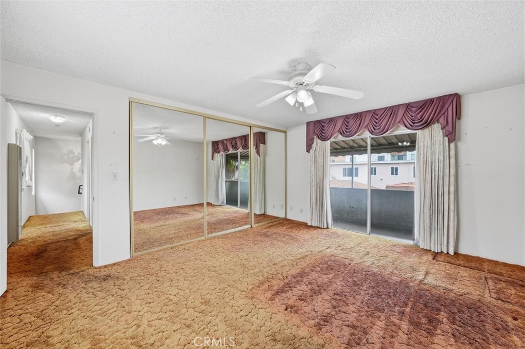 Empty bedroom with mirrored closet doors, patterned carpet, and sliding glass doors to a balcony.