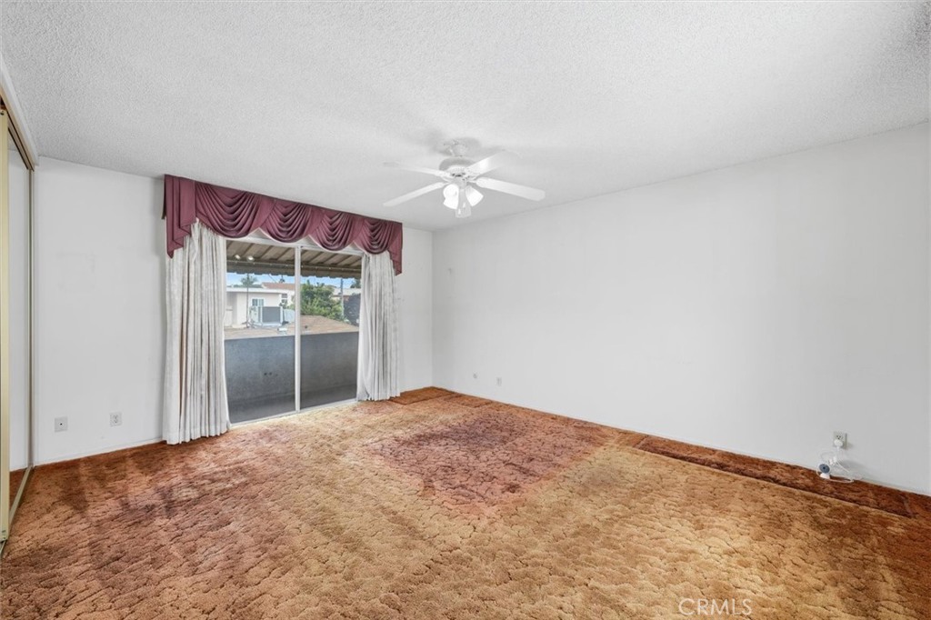 Empty bedroom with rust-colored carpet, a ceiling fan, and a curtained sliding glass door.