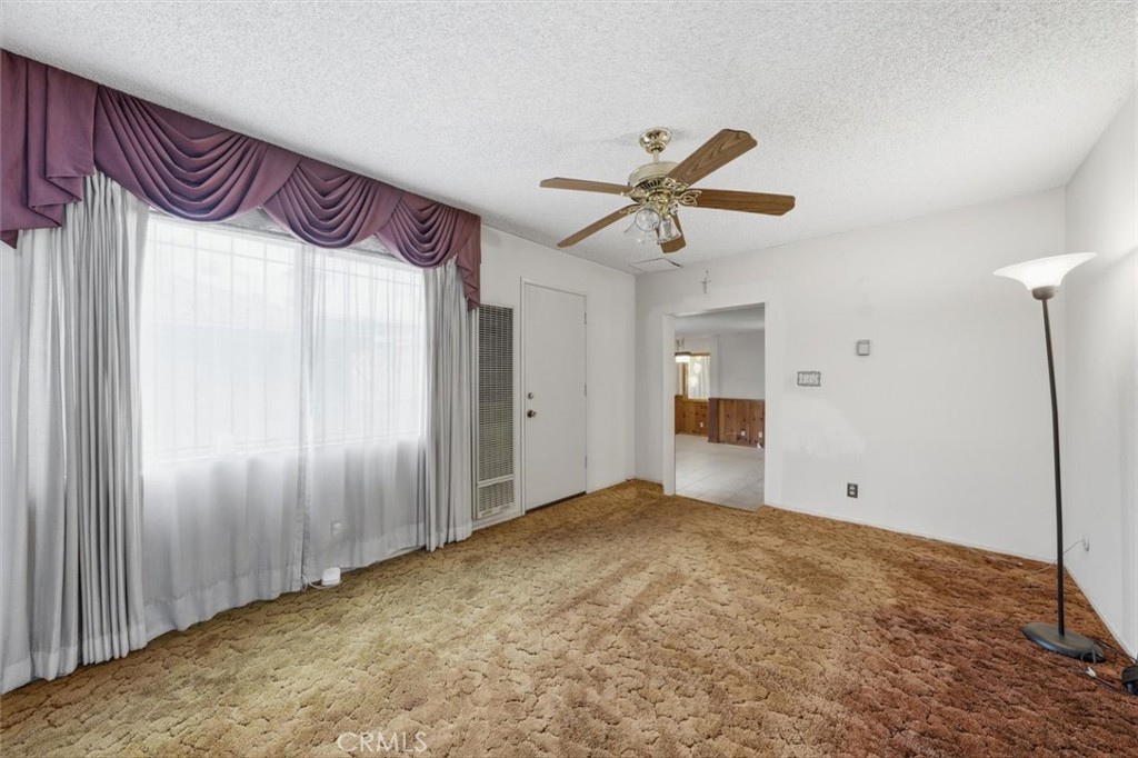 Empty living room with patterned carpet, a large curtained window, and a ceiling fan.