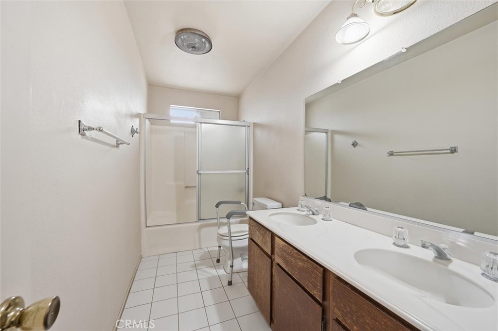 Bathroom with a double-sink wooden vanity, large mirror, and tub with sliding glass enclosure.