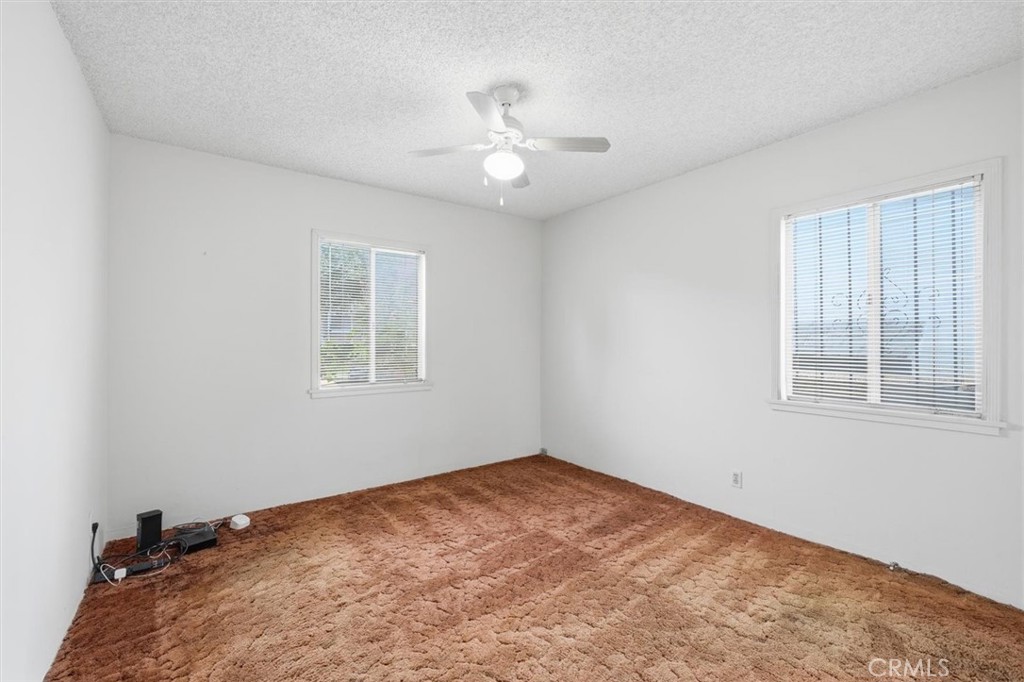 Empty bedroom with brown carpet, two windows with blinds, and a ceiling fan.