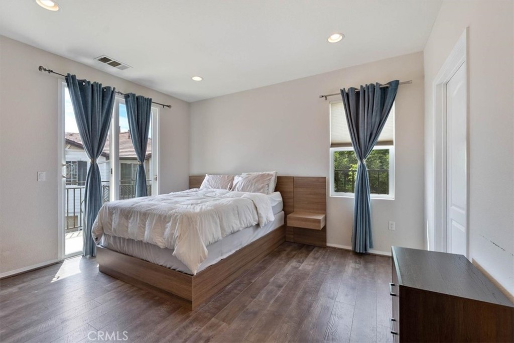 Bedroom with a wood platform bed, hardwood floors, and curtained balcony doors.