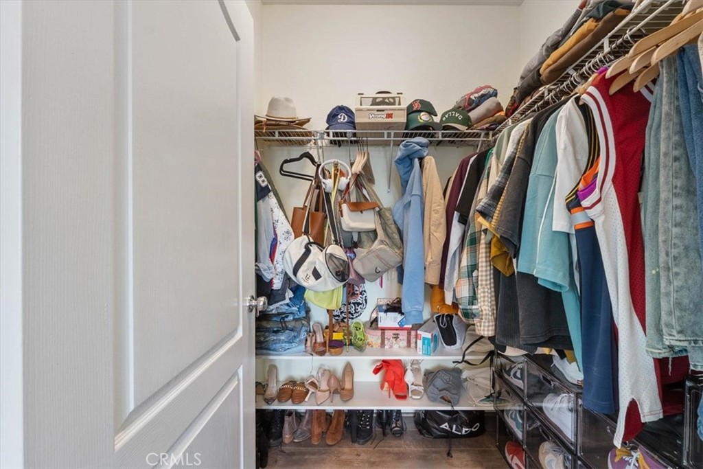 Walk-in closet filled with hanging clothes, hats, handbags, and shoes.