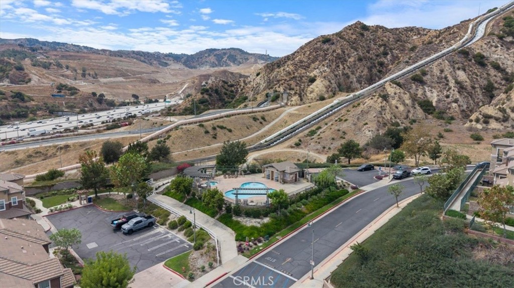 Aerial view of a community pool and homes beside dry hills and a freeway.