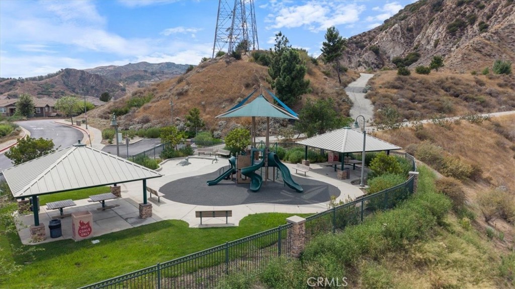 Neighborhood playground with a central slide, shaded picnic pavilions, and dry hills beyond.