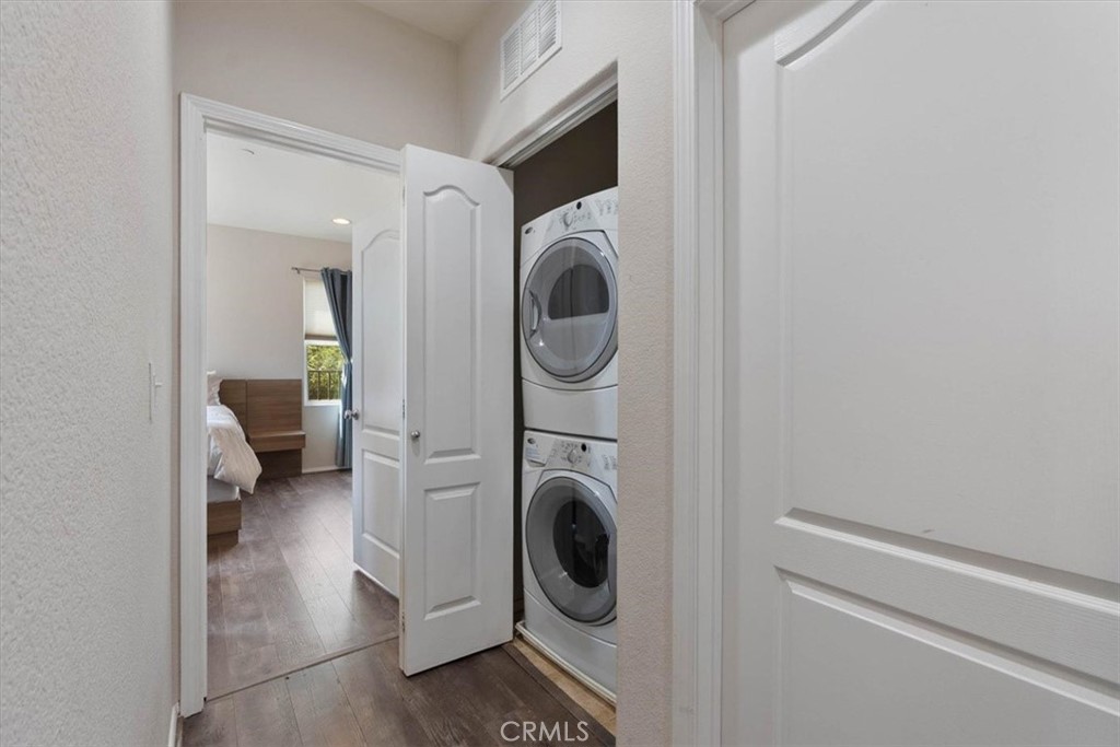 Laundry closet with stacked washer and dryer beside an open doorway to a bedroom.