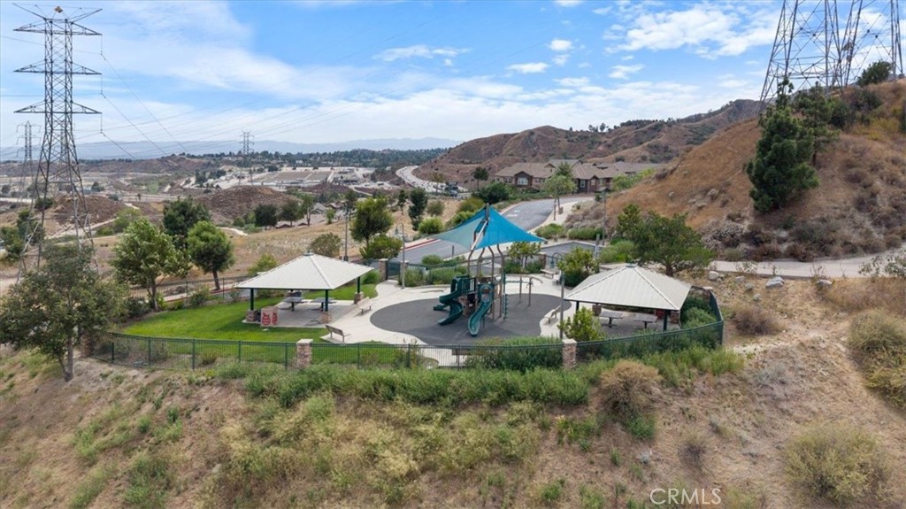 Aerial view of a fenced neighborhood playground with shaded pavilions and surrounding hills.