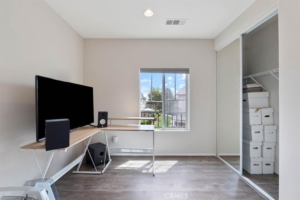 Home office with a desk and monitors beside a window and mirrored closet doors.
