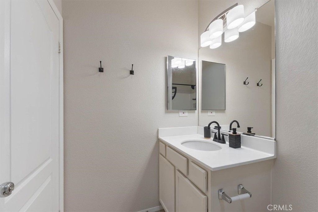 Bathroom vanity with a white countertop, black faucet, large mirror, and modern lighting.