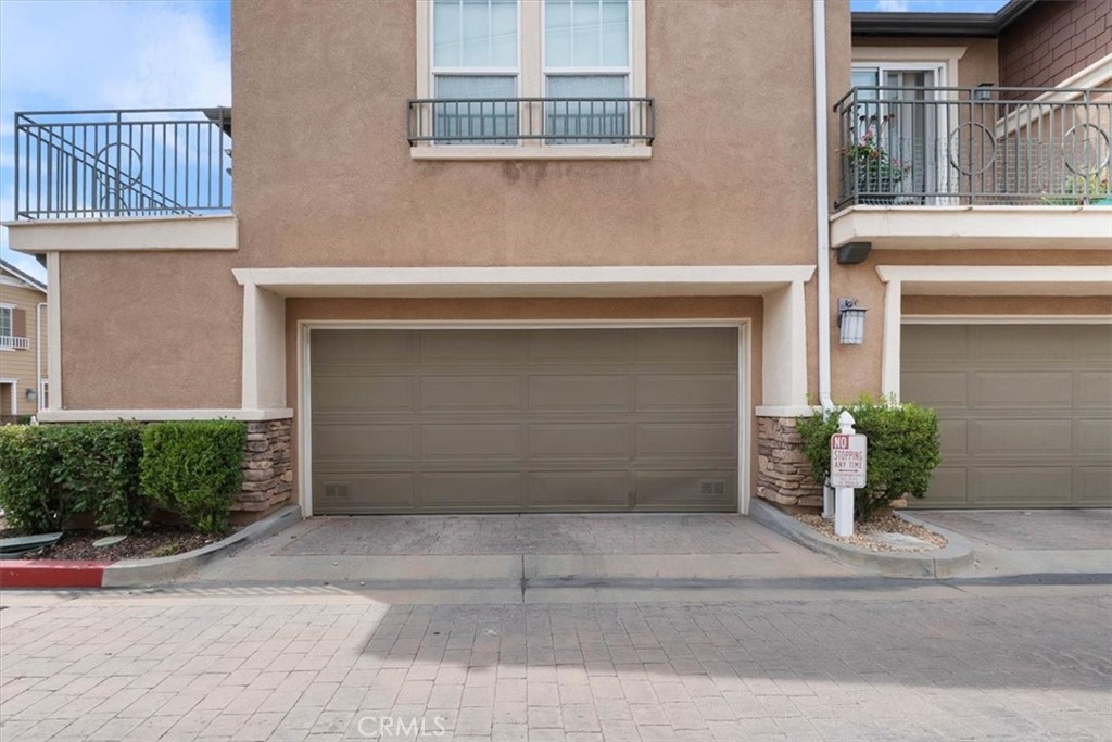 Townhouse exterior with a two-car garage, tan stucco facade, stone accents, and balconies.