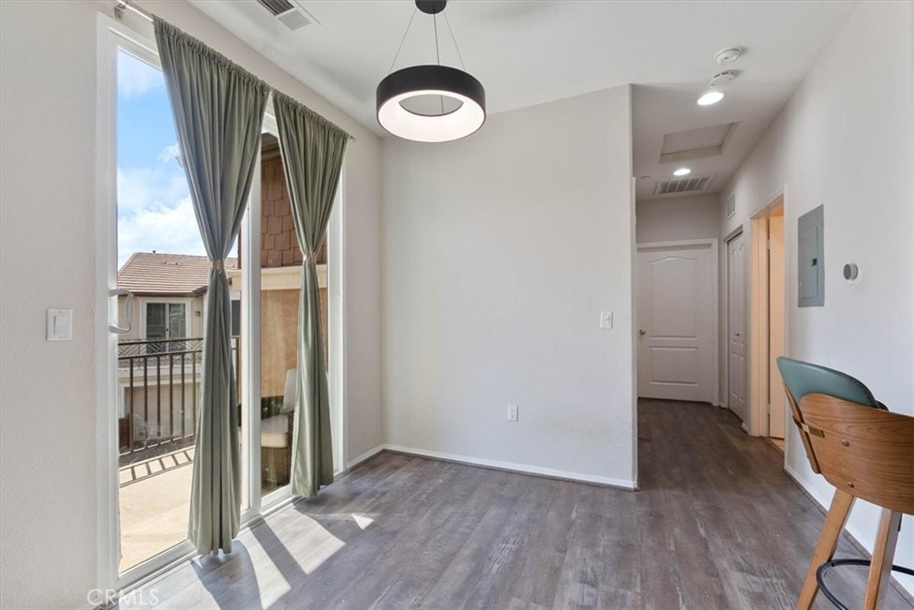 Bright room with balcony doors, gray curtains, wood-look flooring, and a small desk beside the hallway.