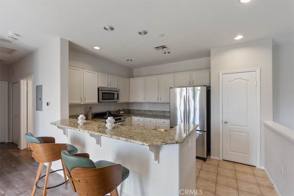 Kitchen with white cabinets, stainless steel appliances, granite counters, and a breakfast bar with wooden stools.