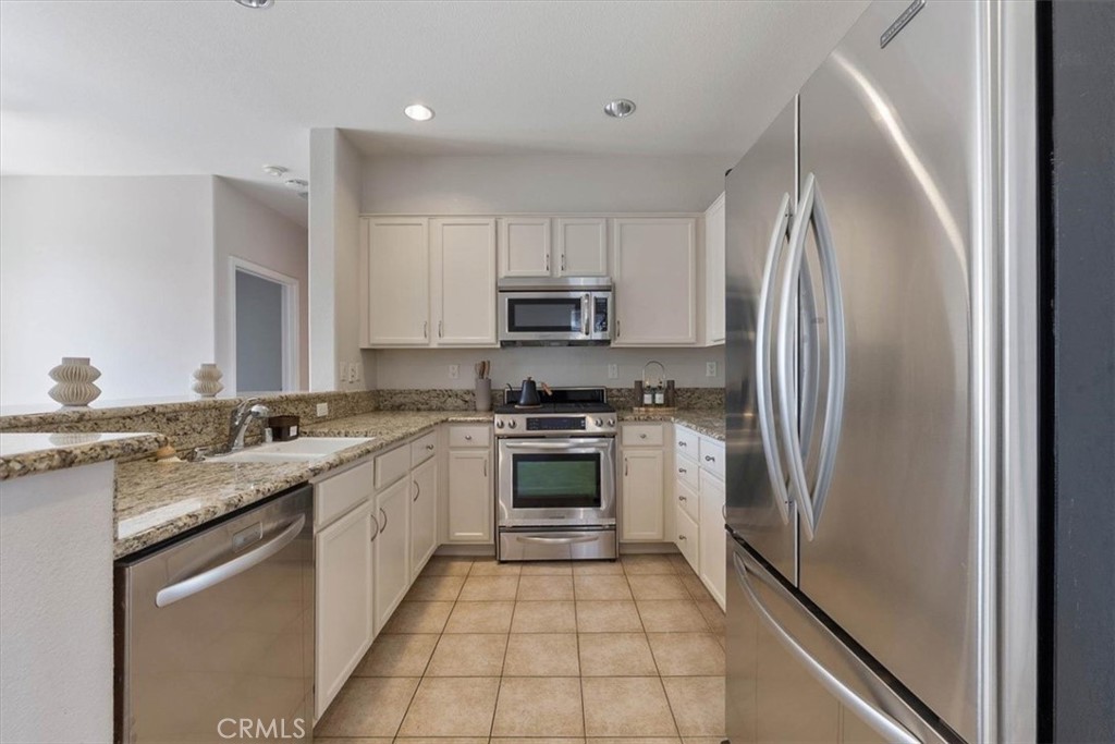 Kitchen with white cabinets, granite counters, stainless steel appliances, and beige tile flooring.