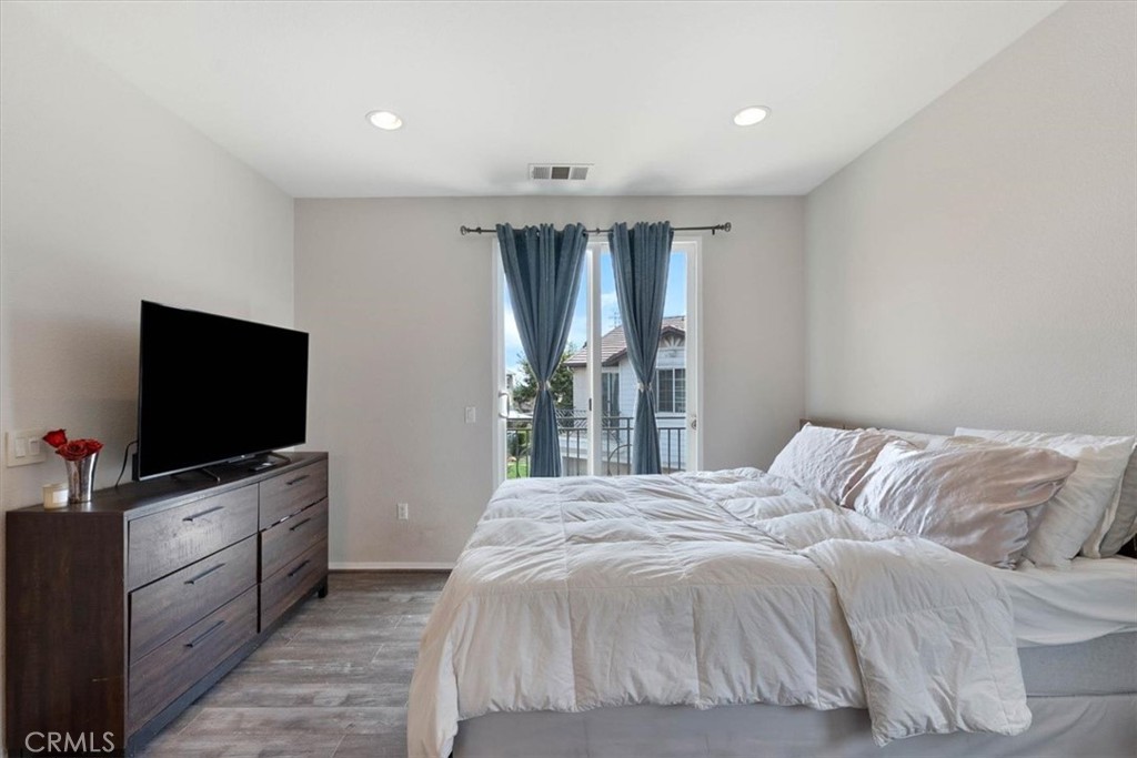 Furnished bedroom with white bedding, blue curtains, and a dresser with television.