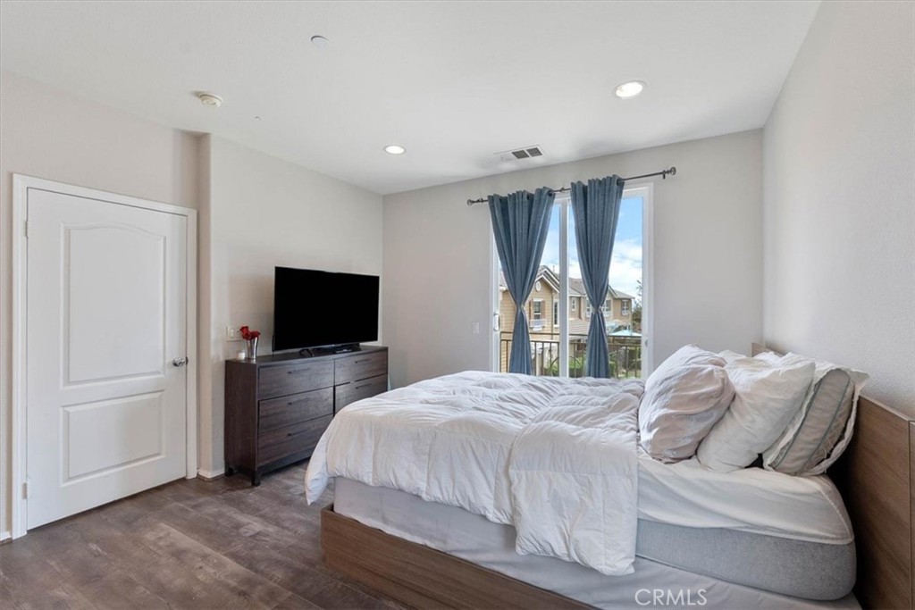 Bedroom with a large bed, wood furniture, and blue curtains framing sliding glass doors to a balcony.