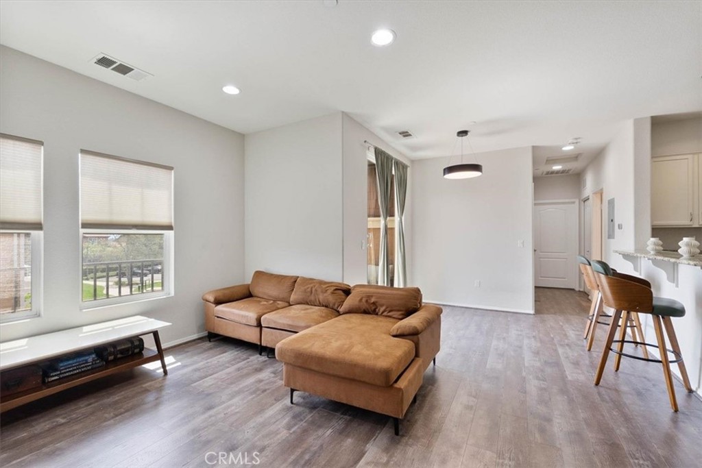 Open-plan living room with a tan sectional, large windows, and a breakfast bar with stools.