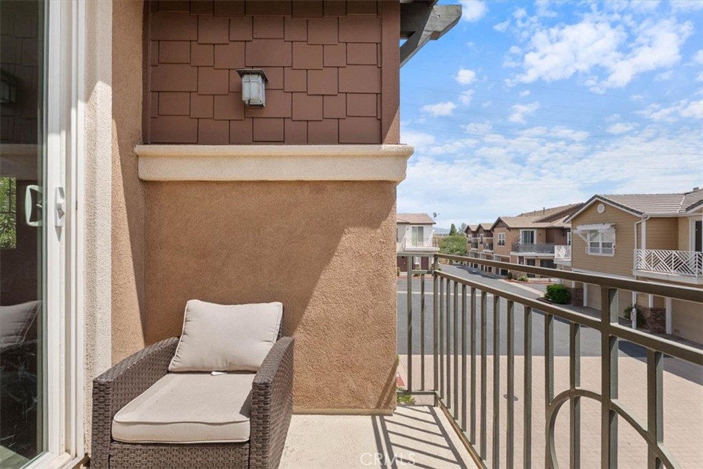 Balcony with a cushioned wicker chaise lounge overlooking nearby homes.